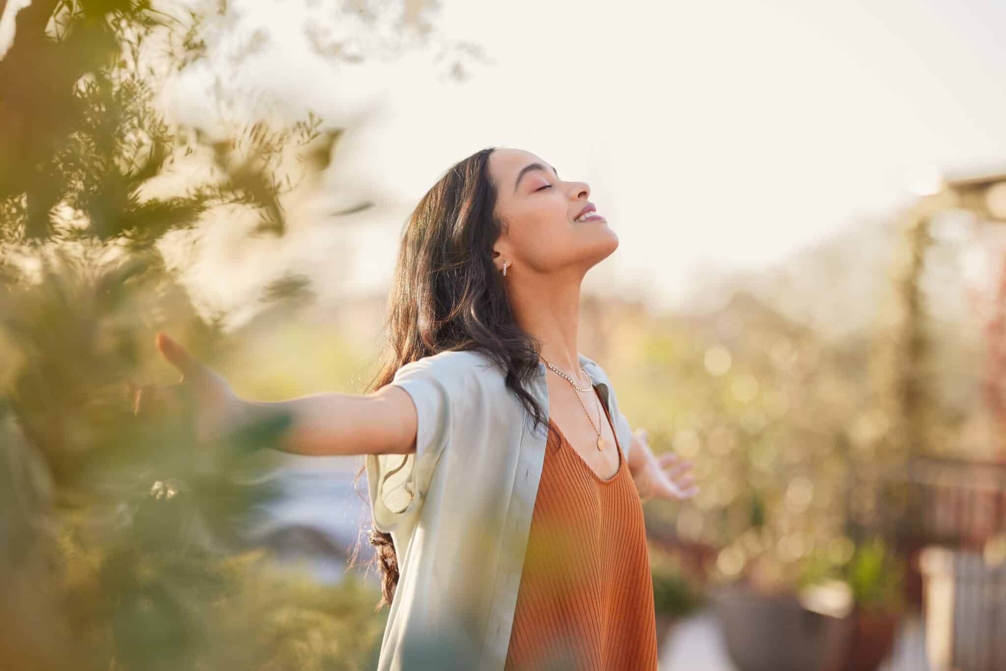 Woman standing outdoors with arms open, eyes closed, breathing deeply, symbolizing clarity, balance, and healing during early addiction recovery.